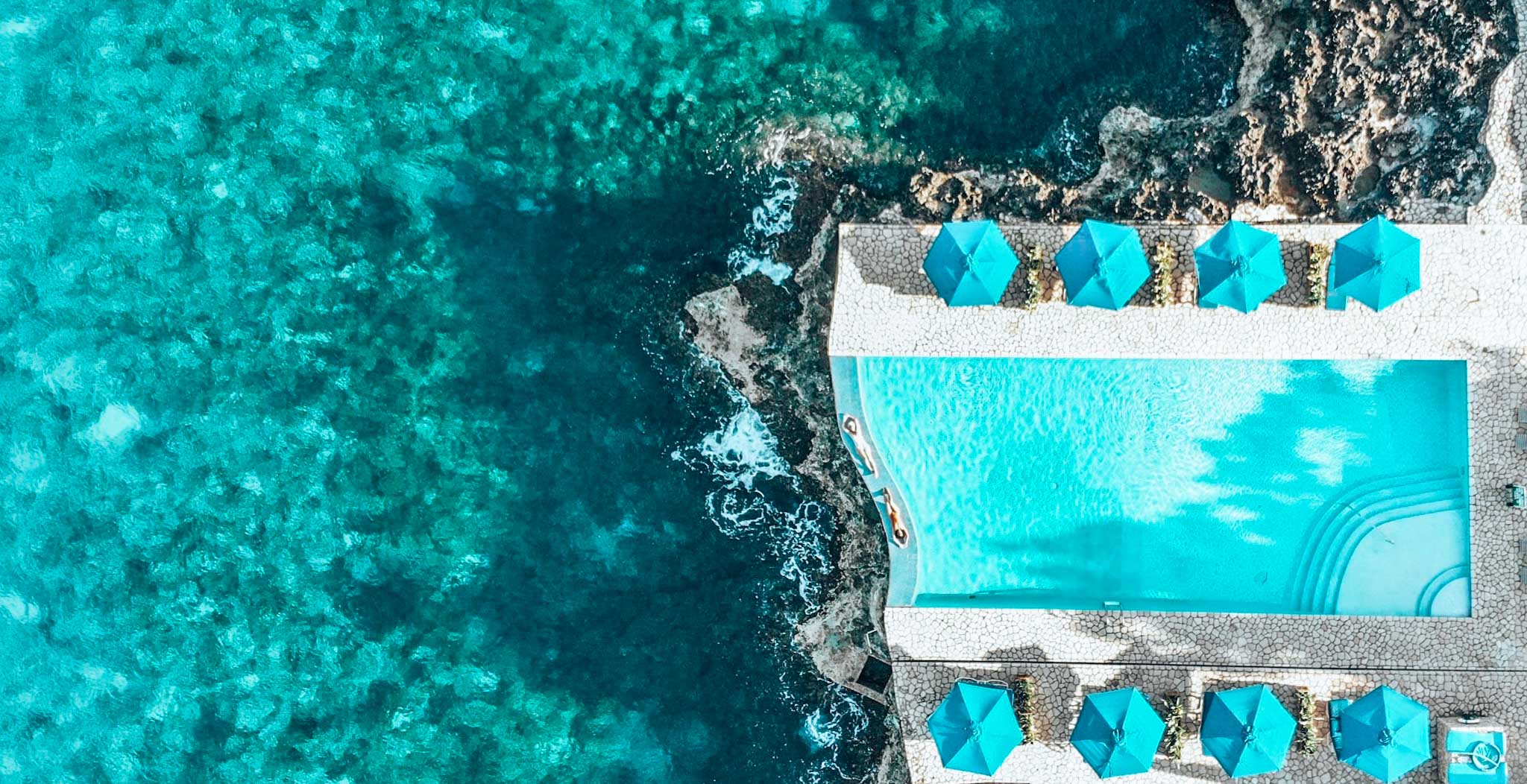 drone photo of two girls lying on the edge of an infinity pool with cliffs and ocean surrounding them