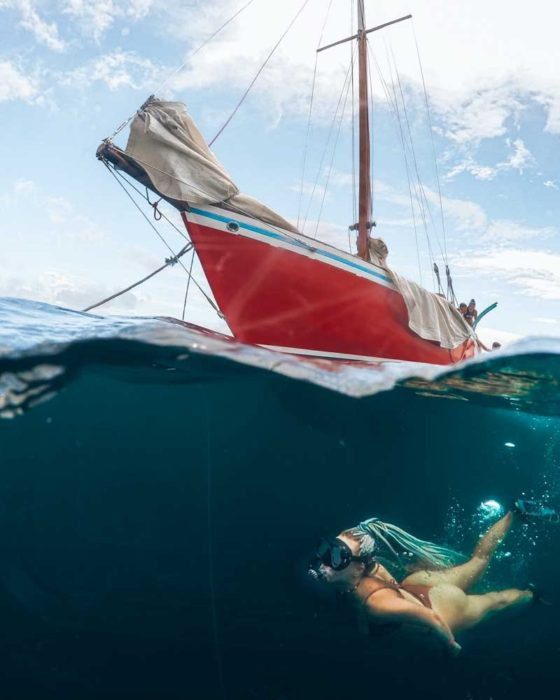 girl snorkelling under a red sailing boat