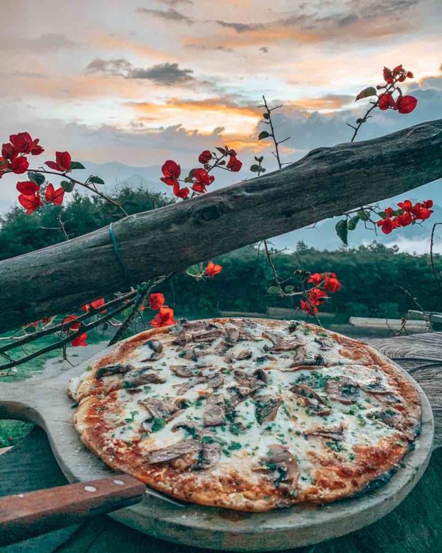 mushroom pizza on a wooden board with sunset clouds in the background