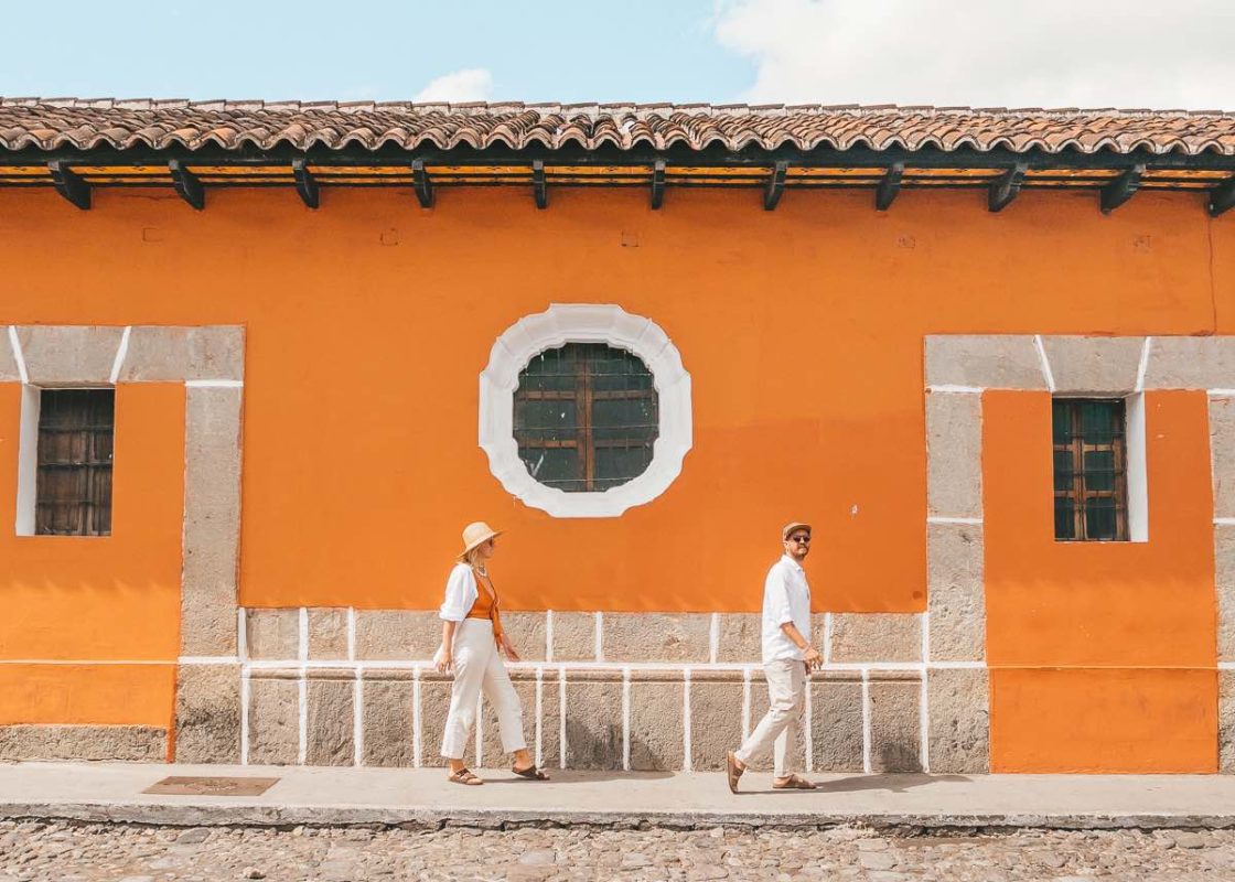 couple walking next to orange coloured building in antigua guatemala