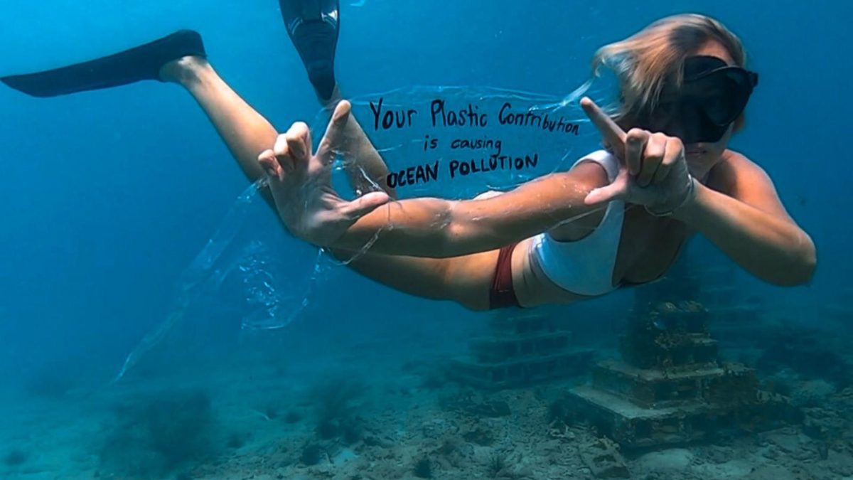 girl swimming underwater holding up a plastic pollution slogan sign