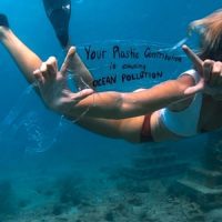 girl swimming underwater holding up a plastic pollution slogan sign