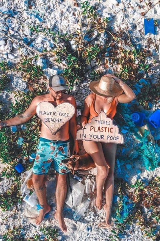 travel couple on the beach surrounded by trash