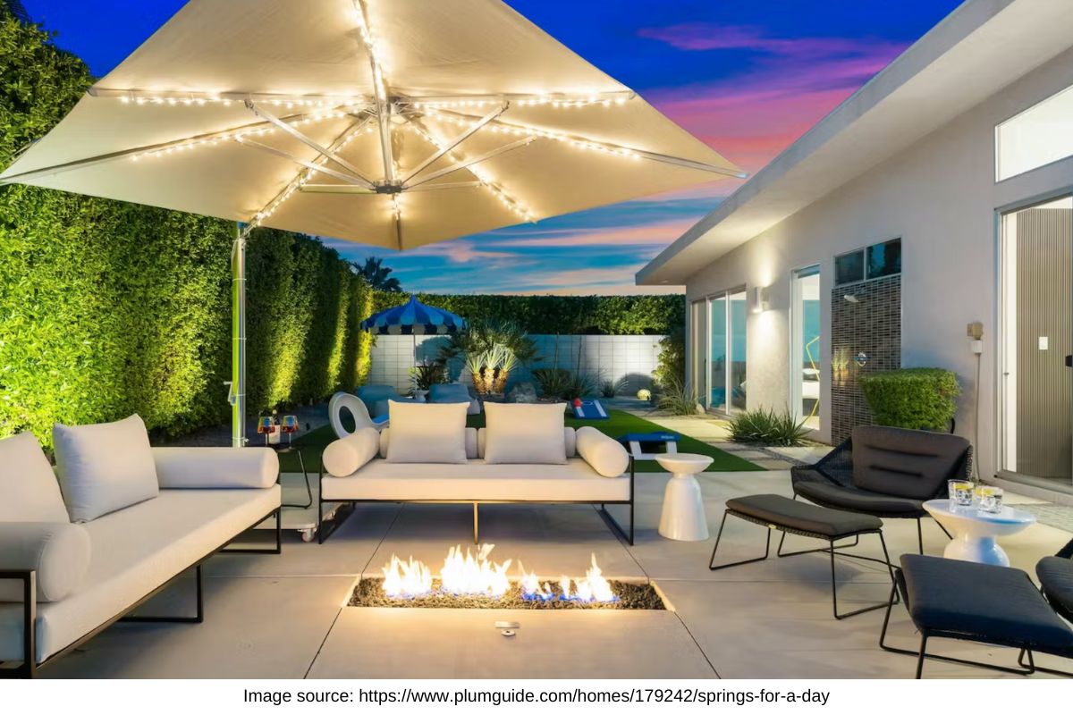 outdoor area with fireplace, green hedge, and umbrella with fairy lights