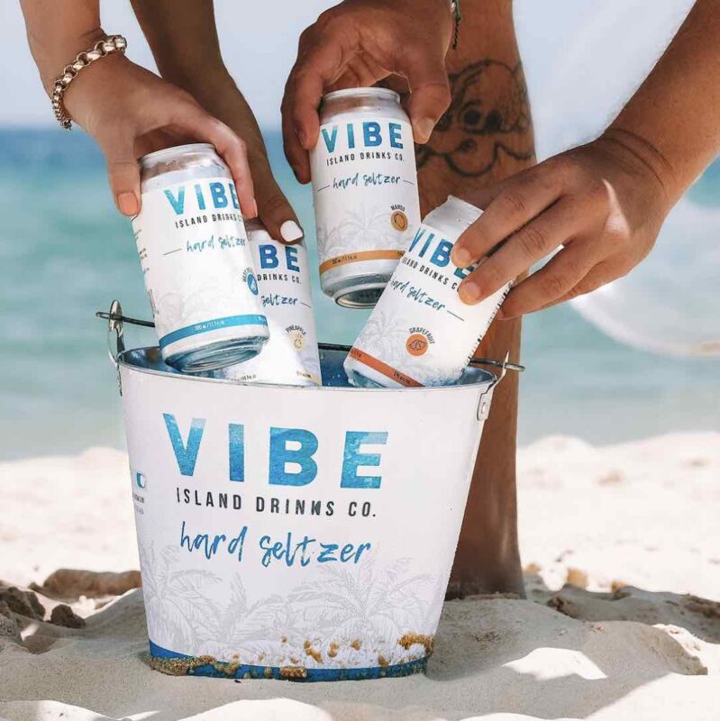 4 flavours of vibe hard seltzer being pulled out of a vibe branded bucket, at the beach