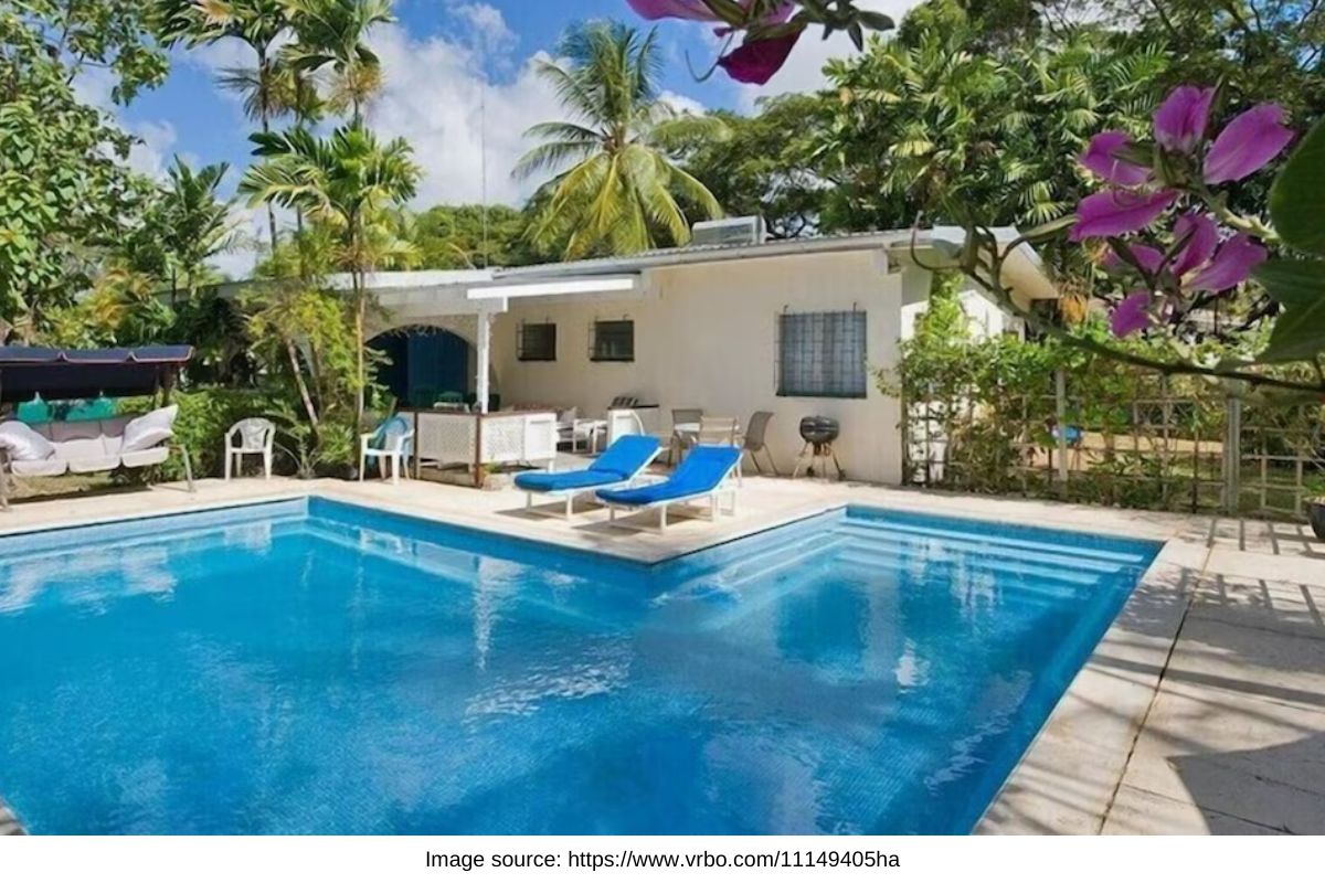 l shaped pool with deck chairs with a home in a tropical garden setting