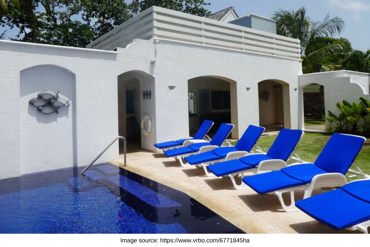 blue pool with blue deck chairs next to a white villa